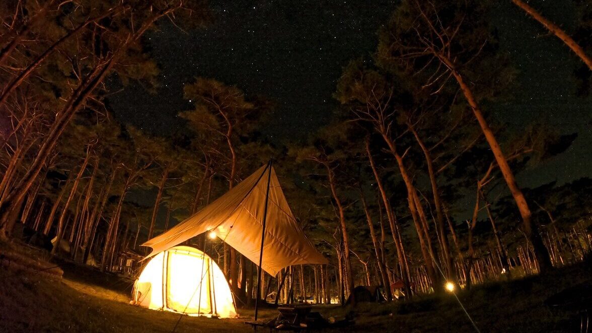 夜にランタンの灯りに照らされたテントとタープ